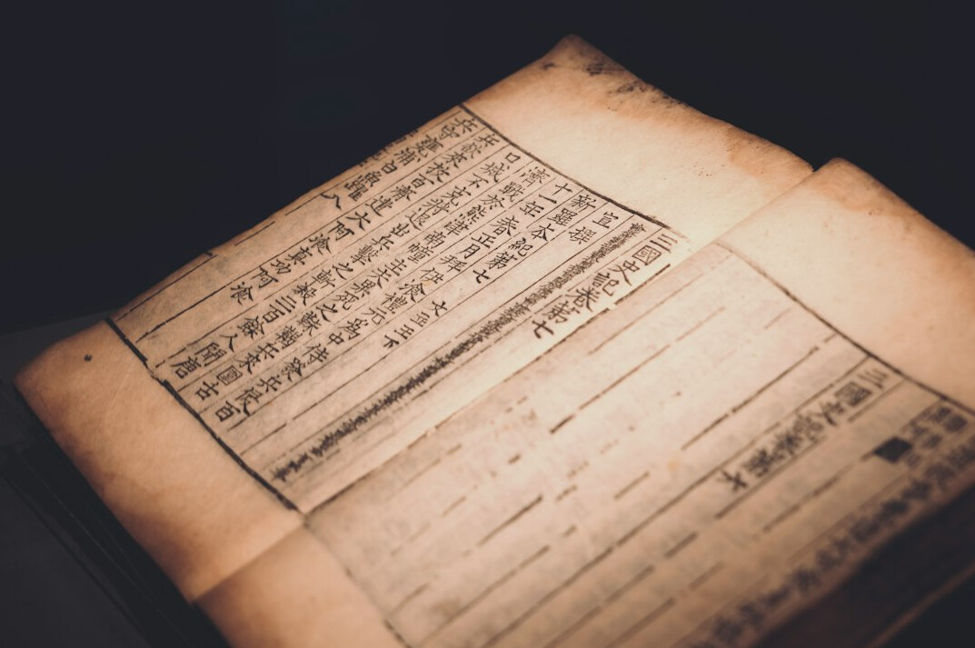 Old documents and photographs spread on a wooden desk with a magnifying glass